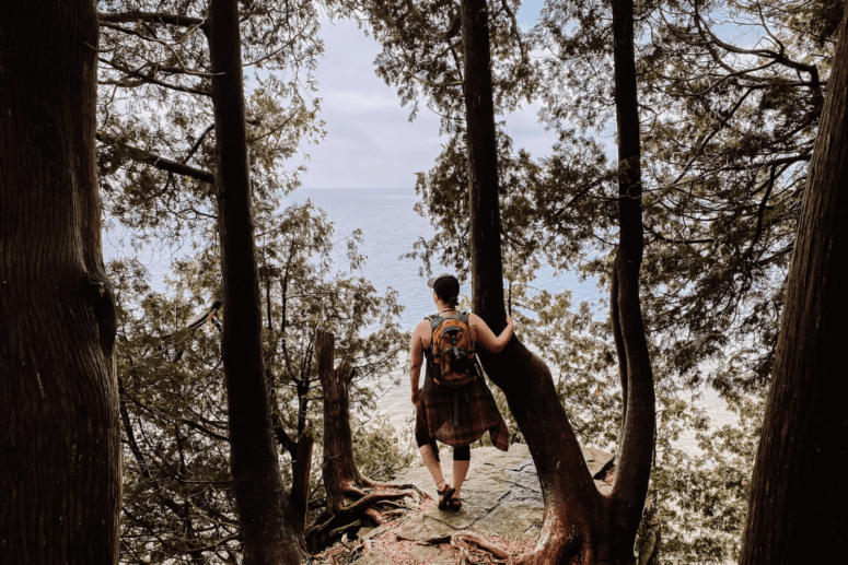 Woman Stands On Cliff Ledge To Overlook Body Of Water