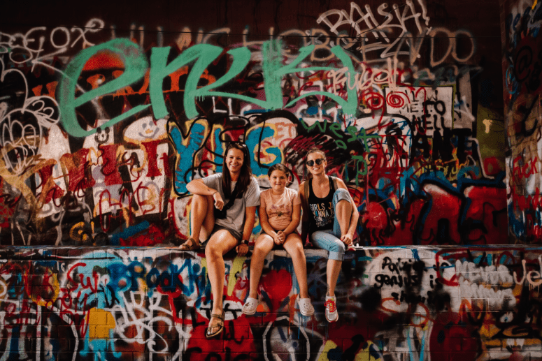 Two Women And A Girl Pose With Graffiti Wall Art