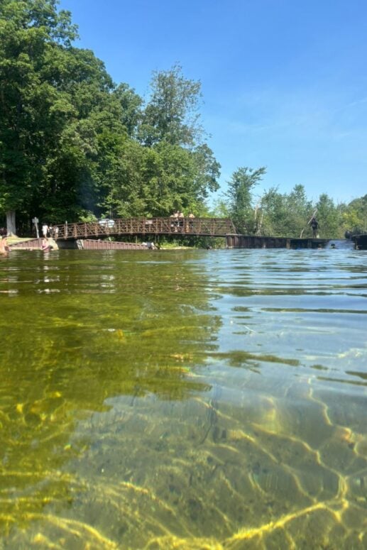The Huron River In The Foreground And A Bridge In The Background At Proud Lake State Recreation Area