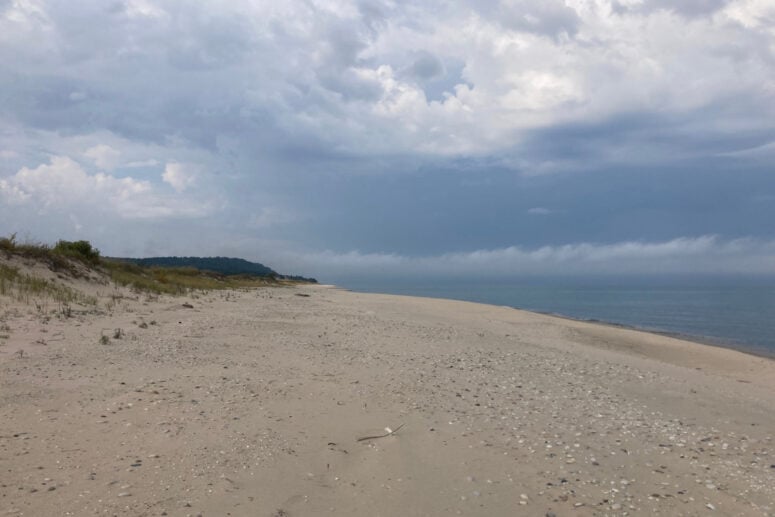On A Beach With Clouds Overhead And The Dunes In The Distance.