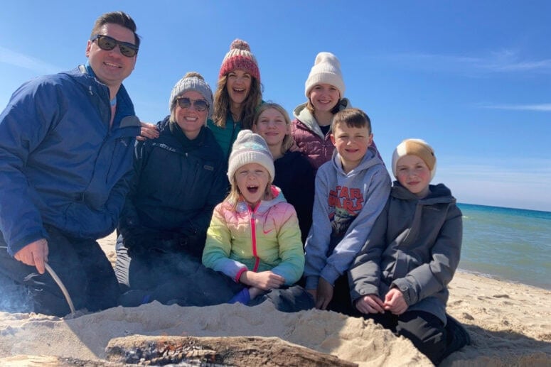 A Group Of Friends Gather Around A Fire On A Cold Day At The Beach.