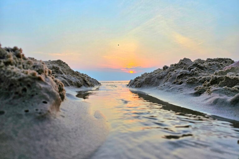 A sunset over a river and beach with rocks lining the water.