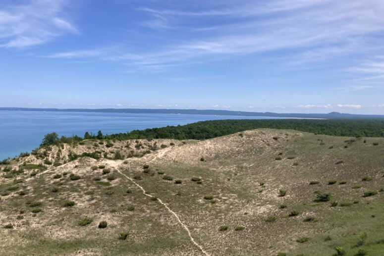 A Sandy Path Winds Over Dunes With Views Of The Water.