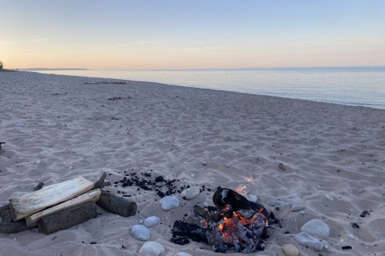 Rocks Lie On A Sandy Beach With A Fire.