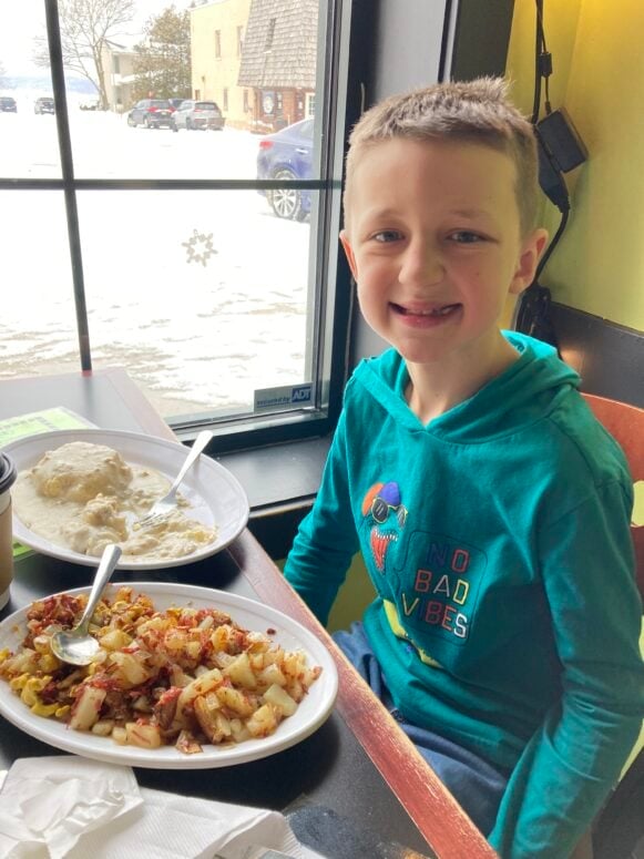A Boy Eating Biscuits And Gravy And Corned Beef Hash In A Diner.