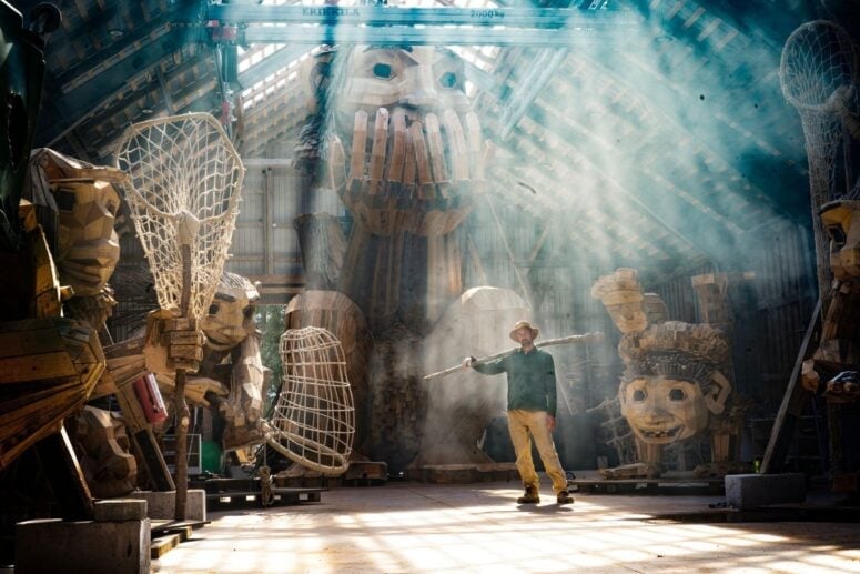 Thomas Dambo In His Workspace Surrounded By Giant Wooden Trolls With Sunlight Filtering In.